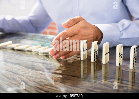 Geschäftsmann Stop Domino auf Schreibtisch Stockfoto