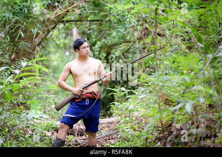 Asiatischer Mann Bauer trägt eine Gewehr Spaziergänge im Wald Hintergrund. Die Jagd und die Lebensweise der ländlichen Bevölkerung in Thailand-Konzept. Stockfoto