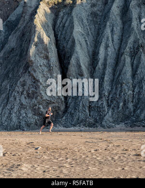 Gesunde Lebensweise. Ein Mann laufen am Strand neben einigen riesigen Klippen in Mwnt, West Wales UK. Stockfoto