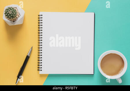 Büro Arbeitsplatz minimalen Begriff. Leer Notebook mit Tasse Kaffee, Kaktus, Bleistift auf gelben und blauen Hintergrund. Ansicht von oben mit der Kopie Raum, flach. Pastellfarben Filter. Stockfoto