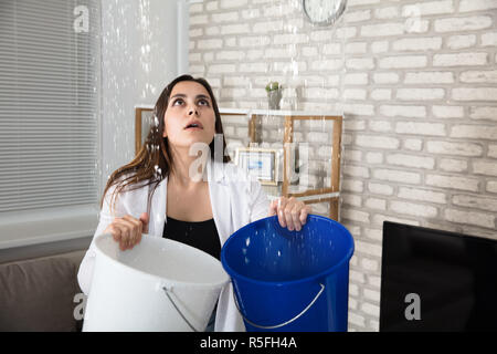 Frau Sammeln austretendes Wasser im Eimer Stockfoto