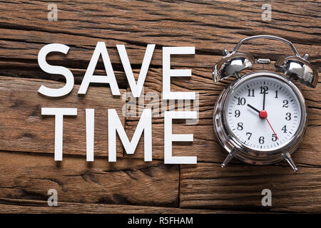 Sparen Sie Zeit Text von Wecker auf hölzernen Tisch Stockfoto
