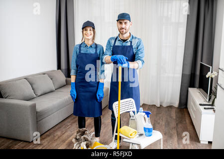 Porträt eines jungen Paares als professioneller Reiniger in der blauen Uniform mit der Reinigung der Werkzeuge in der Wohnung Stockfoto