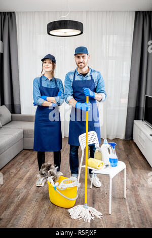Porträt eines jungen Paares als professioneller Reiniger in der blauen Uniform mit der Reinigung der Werkzeuge in der Wohnung Stockfoto