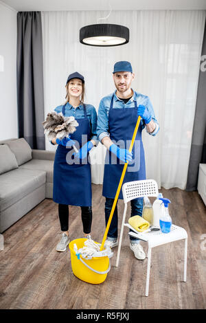 Porträt eines jungen Paares als professioneller Reiniger in der blauen Uniform mit der Reinigung der Werkzeuge in der Wohnung Stockfoto