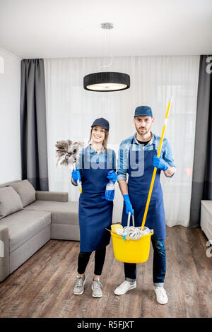 Porträt eines jungen Paares als professioneller Reiniger in der blauen Uniform mit der Reinigung der Werkzeuge in der Wohnung Stockfoto