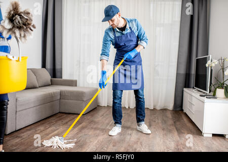Der Mensch als professioneller Reiniger in der blauen Uniform waschen, wischen Stick in der Wohnung gekleidet Stockfoto