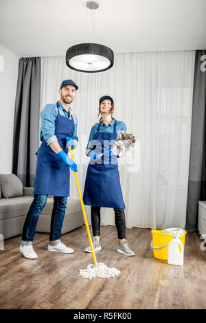 Porträt eines jungen Paares als professioneller Reiniger in der blauen Uniform mit der Reinigung der Werkzeuge in der Wohnung Stockfoto