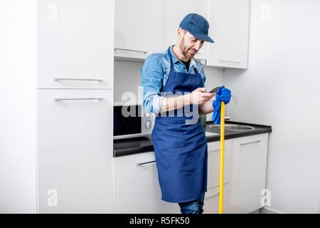 Der Mensch als professioneller Reiniger mit Telefon mit einer Unterbrechung während der Arbeit in der Küche Stockfoto
