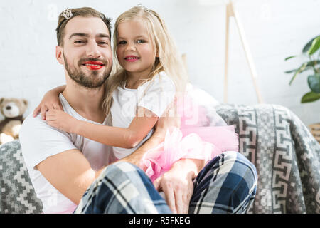 Adorable kleine Tochter im rosa Tutu Rock umarmt glücklich Vater mit roten Lippenstift Stockfoto