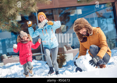 Winter Urlaub. Zeit mit der Familie zusammen im Freien Mann das schneeball Für kämpfen, während Frau und Mädchen läuft auf ihn zu schlagen lächelt Fröhlich Stockfoto