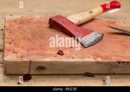 Blutige Holz Schneidebrett auf einem Tisch mit Axt und Messer Stockfoto