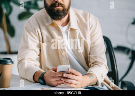 7/8-Ansicht von bärtigen Mann sitzen in Büro und Betrieb smartphone Stockfoto