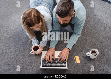 Paar liegend auf dem Boden mit Getränken und online einkaufen Stockfoto