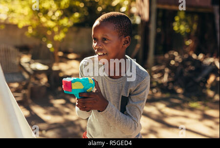 Kleinen afrikanischen Jungen spielen mit Wasser bespritzen Gun im Freien. Kid spielen mit Wasser Gewehr in den Hinterhof. Stockfoto