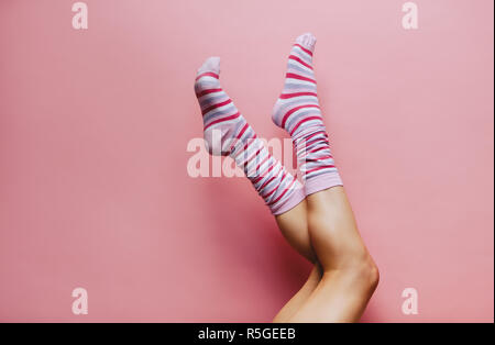 Weibliche Beine in bunten Socken auf rosa Hintergrund. Füße der Frau Socken tragen angehoben. Stockfoto