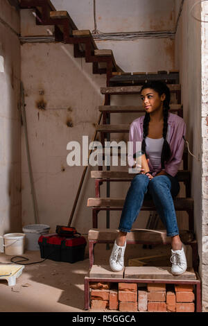 Schöne junge Frau sitzt auf der Treppe mit Papier Tasse Kaffee bei der Renovierung des Home Stockfoto