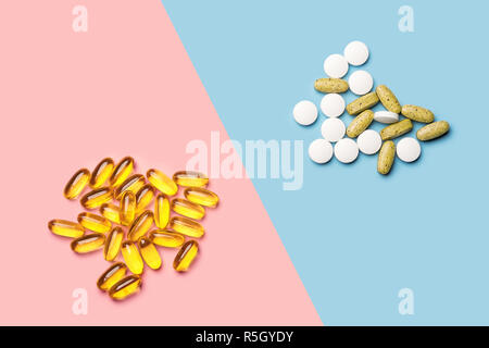 Ein Haufen von weißen und gelben Pillen Vitamine und einen Haufen Gelber Fisch Öl Kapseln auf hell blau und rosa Hintergrund shot mit Studio Licht von oben Stockfoto
