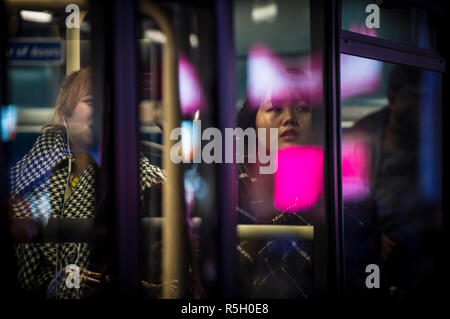 LONDON - November 26, 2018: die Passagiere auf der Rückbank eines öffentlichen Bus reflektiert die bunten blinkenden Werbetafeln in der Nacht im Piccadilly Circus Stockfoto