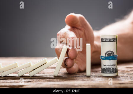 Hand anhalten Dominosteine fallen in Richtung Dollarscheine Stockfoto