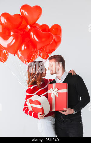 Glücklich küssende Paar in Liebe halten Valentinstag Geschenke und Haufen von Luftballons in Herzform Stockfoto