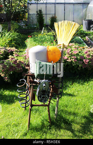 Eine Vogelscheuche aus improvisierten Metallteile mit einem Bau Helm und Garten Besen steht auf dem Gartengrundstück im Garten. Kreative Handarbeit. Russland. Stockfoto