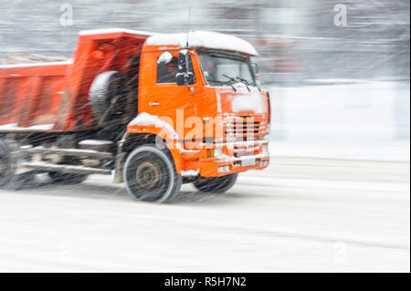 Big Orange Dump Truck fährt auf einer verschneiten Straße während eines Schneesturms. In bewegung Hintergrund verschwommen. Stockfoto