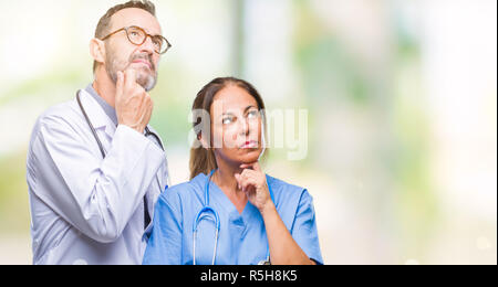 Mittleres Alter spanischer Ärzte Partner Paar mit medizinischen gleichmäßig über isolierte Hintergrund mit der Hand am Kinn über die Frage nachdenken, nachdenklich Expres Stockfoto