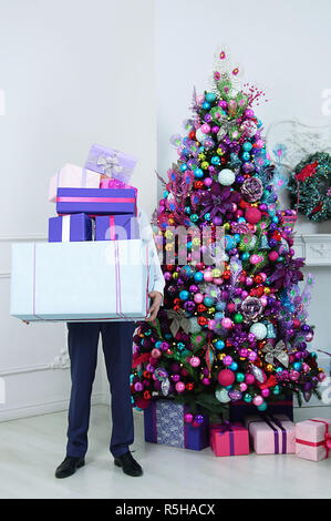 Der Mann hält Kartons mit Geschenken. Neben den Weihnachtsbaum. Stockfoto