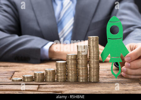 Geschäftsmann Holding Grünbuch Rakete auf Gestapelte Münzen auf Tisch Stockfoto