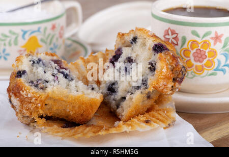 Nahaufnahme einer Blueberry Muffin in der Hälfte mit einer Tasse Kaffee im Hintergrund Stockfoto
