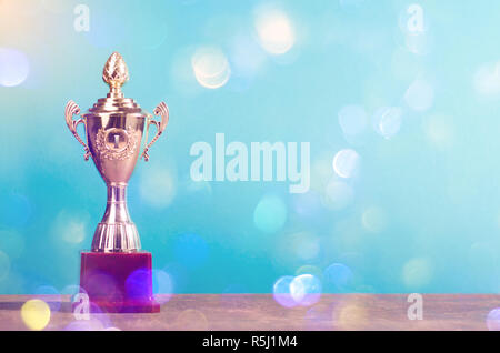 Gewinner der Goldenen Trophäe am Himmel Hintergrund stehen auf hölzernen Schreibtisch festliche Bokeh blur Hintergrund Stockfoto