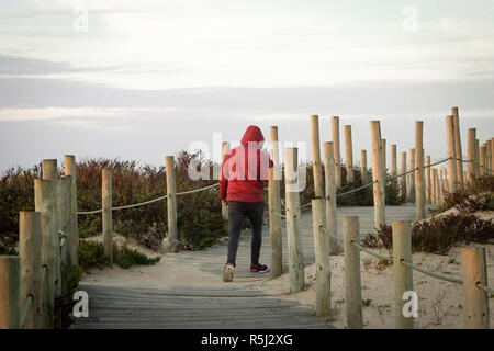 Ansicht der Rückseite ein Mann mit einem roten Winter Jacke entlang eine hölzerne Promenade, beim Beantworten eines Anrufs auf Lautsprecher. Kopieren Sie Platz. Stockfoto