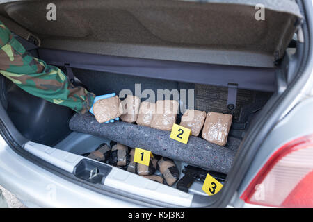 Polizeioffizier holding Droge Paket im Kofferraum eines Autos gefunden Stockfoto