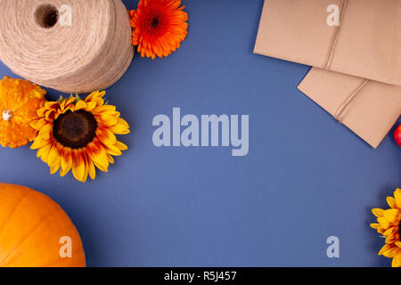 Draufsicht auf das Handwerk Geschenkbox mit gelben und orangen Blüten, Seil, Haspel und Kürbisse auf blauem Hintergrund. Leere Grußkarte für kreative Arbeit Design. Flach Stockfoto