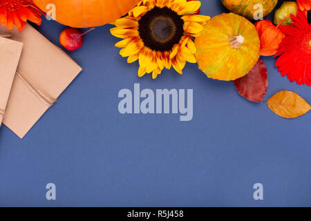 Draufsicht auf das Handwerk Geschenkbox mit gelben und orangen Blüten, Seil, Haspel und Kürbisse auf blauem Hintergrund. Leere Grußkarte für kreative Arbeit Design. Flach Stockfoto