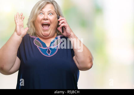 Senior Plus size kaukasische Frau am Telefon zu sprechen über isolierte Hintergrund sehr glücklich und aufgeregt, Sieger Ausdruck feiern Sieg schreien Stockfoto