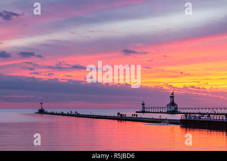 Die untergehende Sonne malt die Himmel über Lake Michigan in herrlichen Farben und Silhouetten der Leuchttürme und Schaulustige auf der North und South Pier in St. Stockfoto