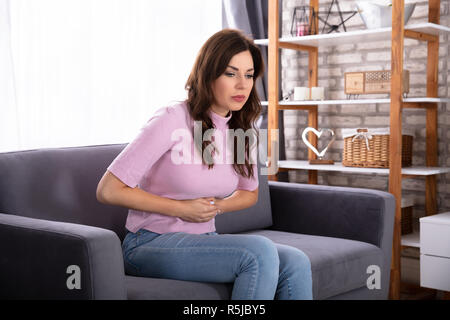 Junge Frau sitzt auf einem Sofa Leiden von Magenschmerzen Stockfoto