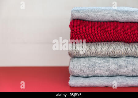 Vier grauen und einem roten gefaltet gestrickte Pullover Verlegung auf rote Fläche. Stockfoto