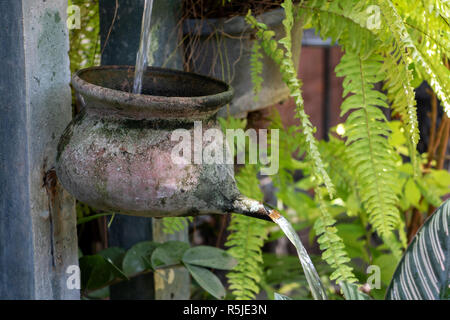 Wasserkaskade aus Töpfen auf Säule mit fließendem Wasser in einem tropischen Garten, Thailand. Garten Brunnen mit Stockfoto