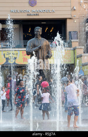 Johannesburg, Südafrika, 1. Dezember 2018. Kinder spielen in den Brunnen in der Nähe der Statue in Nelson Mandela Nelson Mandela Square in Sandton. Südafrika ist derzeit die Feier des 100. Jahrestages der Madiba Geburt. Credit: Eva-Lotta Jansson/Alamy leben Nachrichten Stockfoto