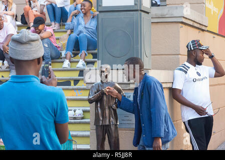 Johannesburg, Südafrika, 1. Dezember 2018. Ein Mann hat Freude daran, eine selfie mit einer Miniatur Nelson Mandela Statue, neben der größeren, in Nelson Mandela Square in Sandton. Südafrika ist derzeit die Feier des 100. Jahrestages der Madiba Geburt. Credit: Eva-Lotta Jansson/Alamy leben Nachrichten Stockfoto