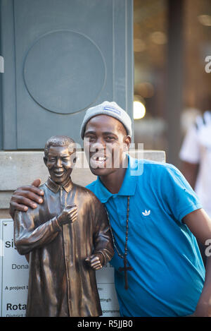 Johannesburg, Südafrika, 1. Dezember 2018. Ein Mann hat Freude daran, eine selfie mit einer Miniatur Nelson Mandela Statue, neben der größeren, in Nelson Mandela Square in Sandton. Südafrika ist derzeit die Feier des 100. Jahrestages der Madiba Geburt. Credit: Eva-Lotta Jansson/Alamy leben Nachrichten Stockfoto