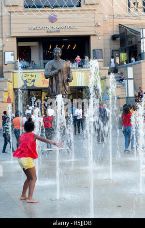 Johannesburg, Südafrika, 1. Dezember 2018. Kinder spielen in den Brunnen in der Nähe der Statue in Nelson Mandela Nelson Mandela Square in Sandton. Südafrika ist derzeit die Feier des 100. Jahrestages der Madiba Geburt. Credit: Eva-Lotta Jansson/Alamy leben Nachrichten Stockfoto