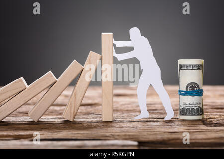 Papier Mann stoppen Holz- Domino Bausteine durch Hundert-Euro-Scheine Stockfoto