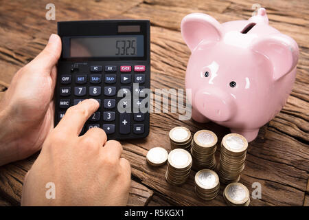 Geschäftsmann mit Rechner von Münzen und Sparschwein auf Tisch Stockfoto