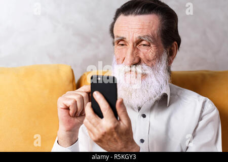 Stattlichen älteren bärtigen Mann mit weißem T-Shirt gelb sitzen auf dem Sofa und schreiben Nachricht Stockfoto