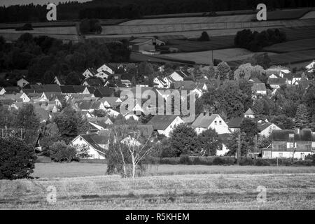 Blick auf die kleine Stadt Neustadt (Landkreis Marburg-Biedenkopf in Hessen), die Vororte und die umliegenden landwirtschaftlichen Flächen in der Morgensonne. Schwarz und Weiß. Stockfoto