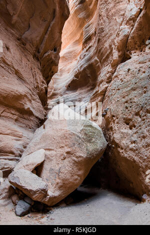 Ein riesiger Felsblock liegt im Boden eines tiefen Slot Canyon underheath ein Canyon Wand Tageslicht von oben, aus Kasha-Katuwe Tent Rocks National Mo widerspiegelt Stockfoto